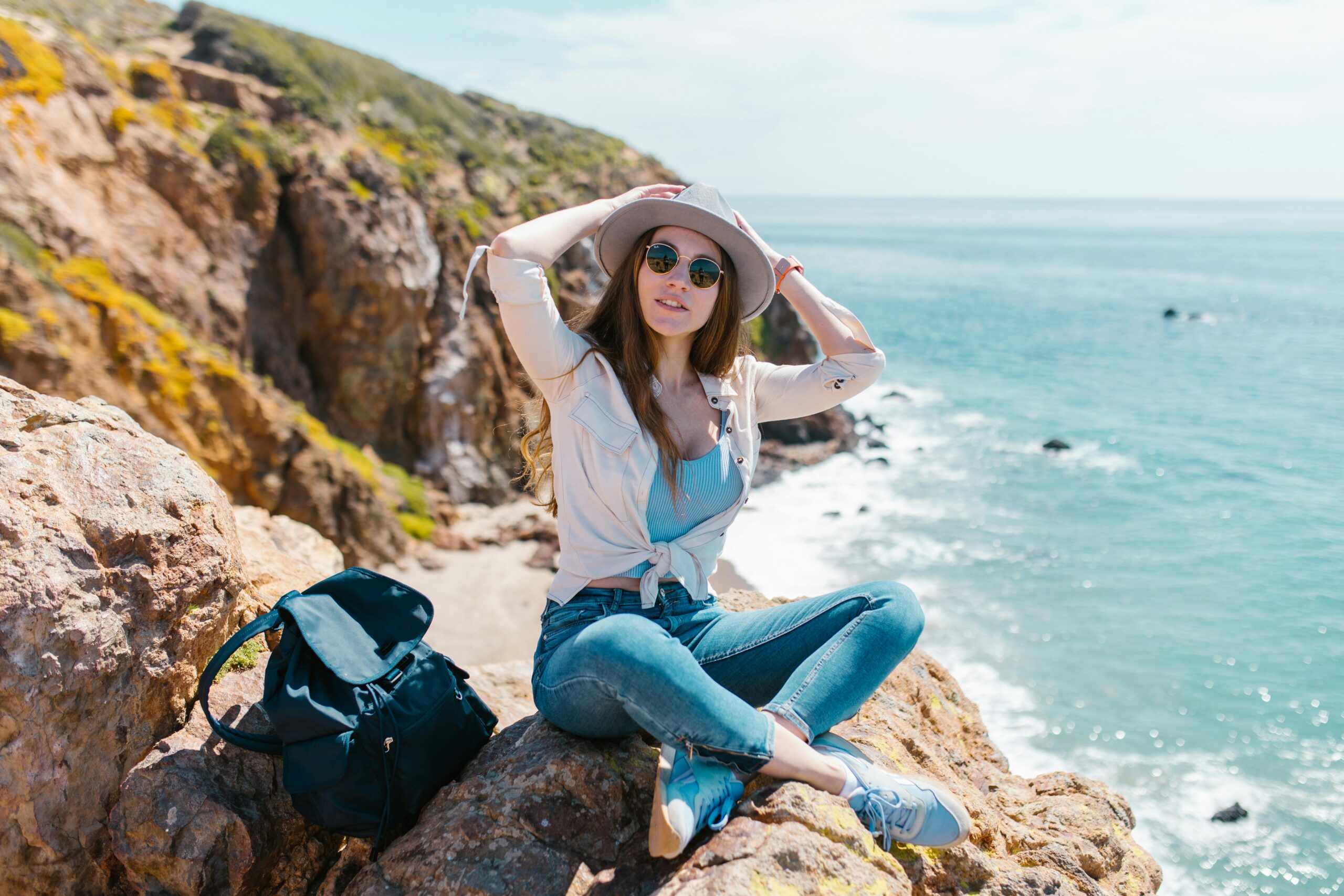 Young woman enjoying a sunny day by rocky beach, embracing the outdoor adventure spirit.